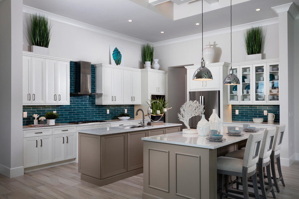 Inspiration for a beach style kitchen in Miami with an undermount sink, glass-front cabinets, white cabinets, blue splashback, subway tile splashback, stainless steel appliances, multiple islands, beige floor and white benchtop.