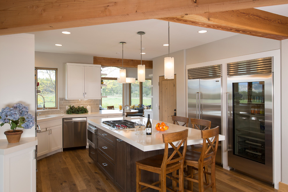Inspiration for a mid-sized rustic u-shaped medium tone wood floor eat-in kitchen remodel in Albuquerque with a farmhouse sink, flat-panel cabinets, white cabinets, marble countertops, gray backsplash, porcelain backsplash, stainless steel appliances and an island