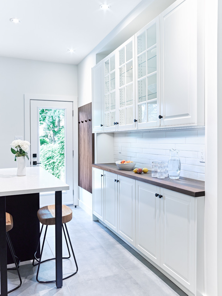 Enclosed kitchen - mid-sized transitional galley porcelain tile and gray floor enclosed kitchen idea in Toronto with an undermount sink, recessed-panel cabinets, white cabinets, wood countertops, white backsplash, subway tile backsplash, stainless steel appliances and an island