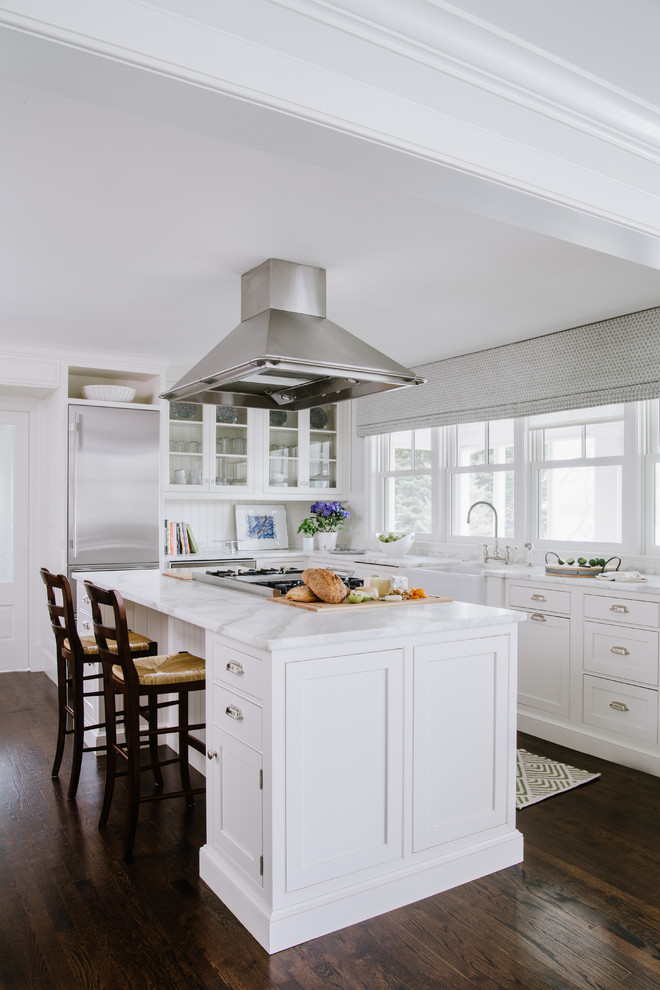 Beach style l-shaped kitchen in Baltimore with a farmhouse sink, shaker cabinets, white cabinets, marble benchtops, white splashback, stainless steel appliances, with island, white benchtop, dark hardwood floors and brown floor.