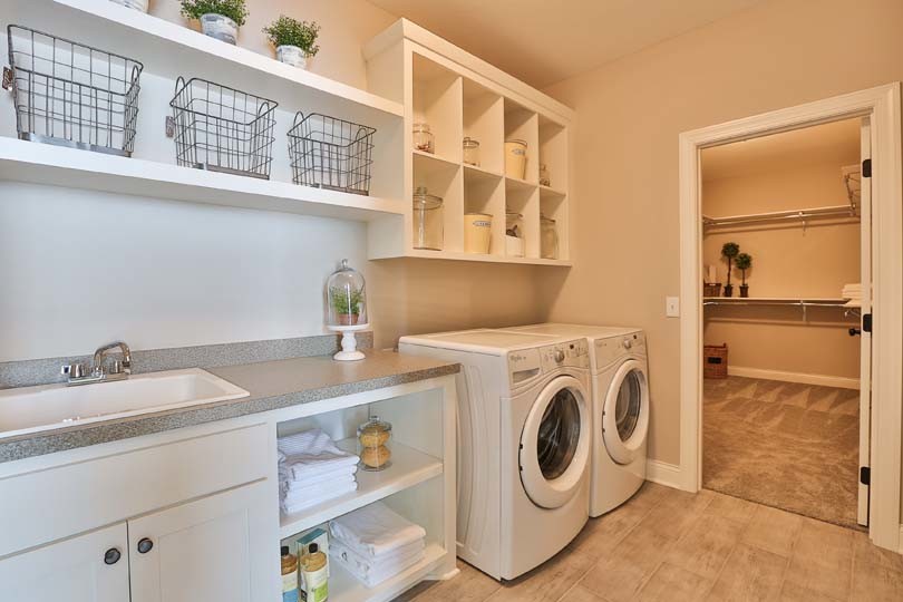 This is an example of a mid-sized traditional single-wall utility room in Minneapolis with a drop-in sink, open cabinets, white cabinets, laminate benchtops, beige walls, vinyl floors and a side-by-side washer and dryer.