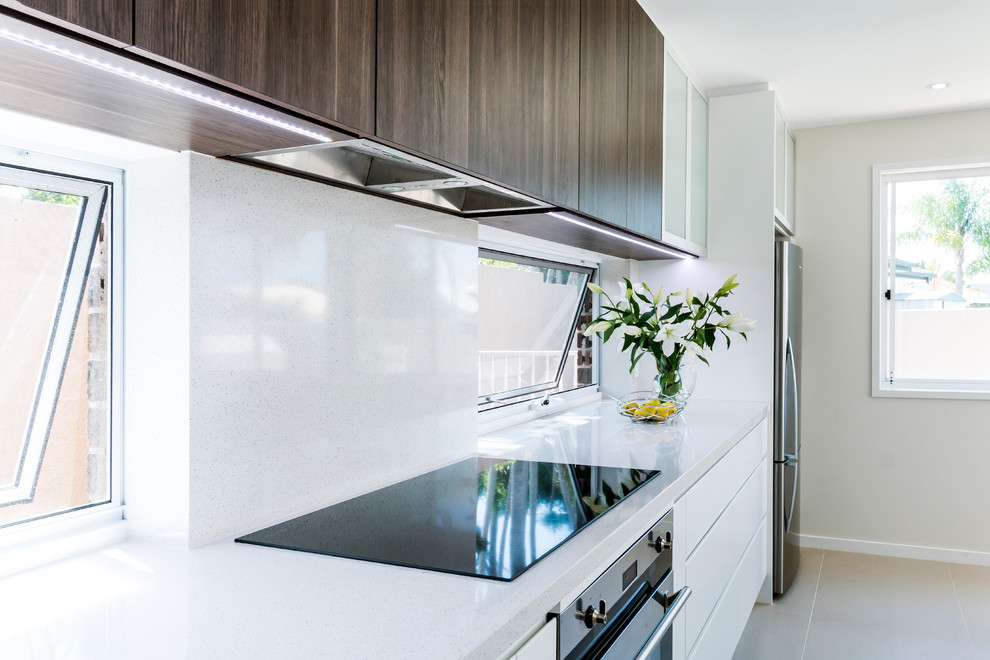 Photo of a large contemporary galley kitchen in Gold Coast - Tweed with a double-bowl sink, flat-panel cabinets, dark wood cabinets, quartz benchtops, stone slab splashback, stainless steel appliances, porcelain floors and with island.