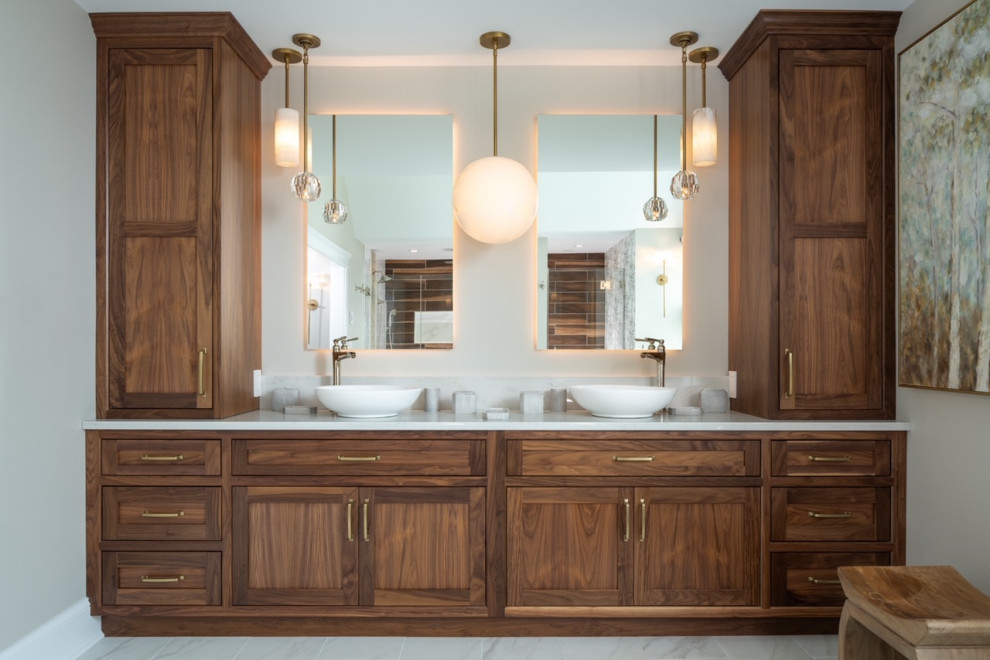 This is an example of a large transitional master bathroom in Philadelphia with raised-panel cabinets, medium wood cabinets, a freestanding tub, a double shower, a two-piece toilet, white tile, marble, grey walls, marble floors, a vessel sink, engineered quartz benchtops, white floor, a hinged shower door, white benchtops, an enclosed toilet, a double vanity, a built-in vanity, exposed beam and wallpaper.