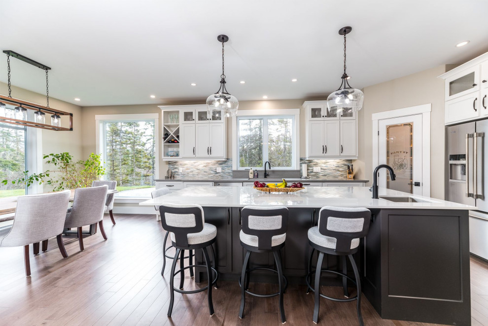 Example of a mid-sized transitional medium tone wood floor and brown floor open concept kitchen design with an undermount sink, shaker cabinets, white cabinets, granite countertops, gray backsplash, mosaic tile backsplash, stainless steel appliances, an island and gray countertops