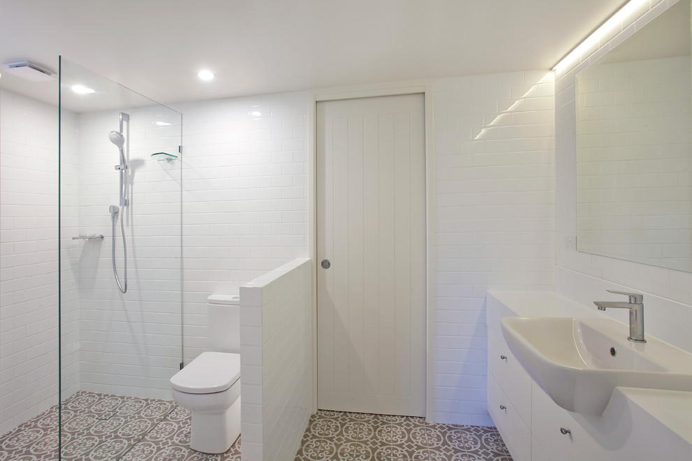 This is an example of a mid-sized beach style master bathroom in Sunshine Coast with white cabinets, a drop-in tub, a corner shower, multi-coloured tile, ceramic tile, white walls, ceramic floors and a wall-mount sink.