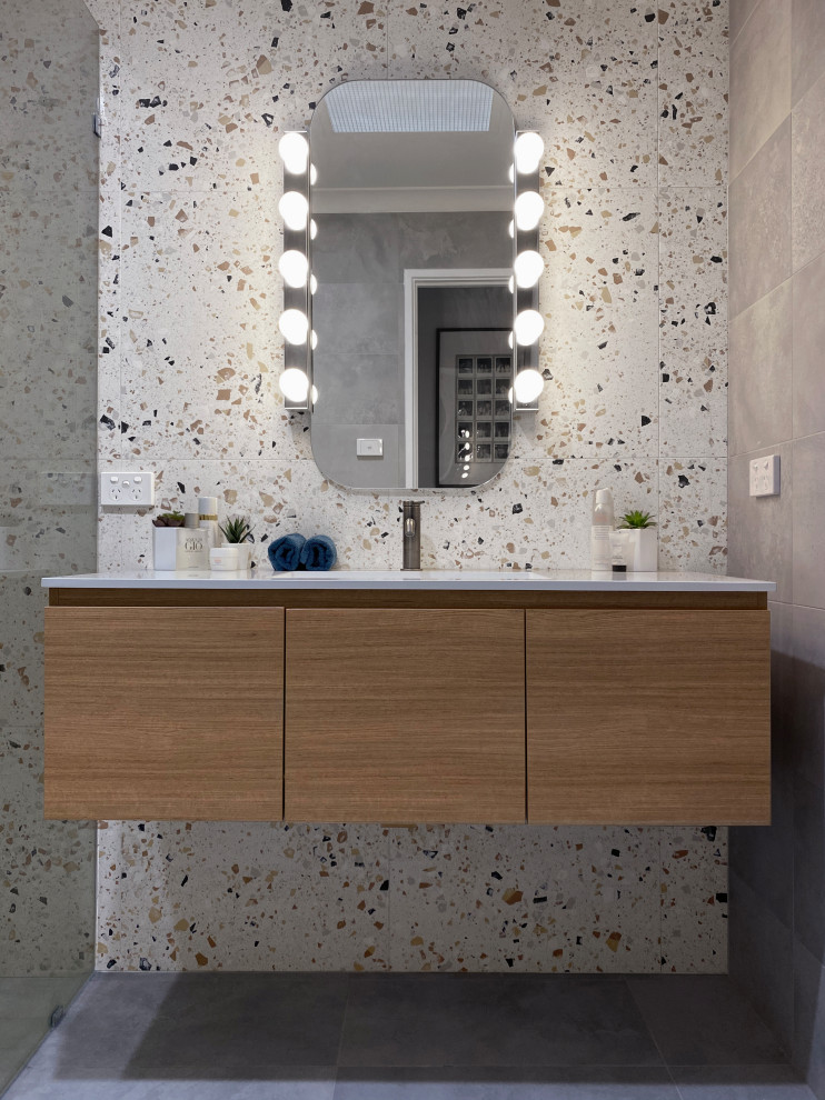 This is an example of a mid-sized contemporary master bathroom with flat-panel cabinets, medium wood cabinets, an open shower, a one-piece toilet, multi-coloured tile, porcelain tile, purple walls, porcelain floors, an integrated sink, engineered quartz benchtops, grey floor, an open shower, white benchtops, a niche, a single vanity and a floating vanity.