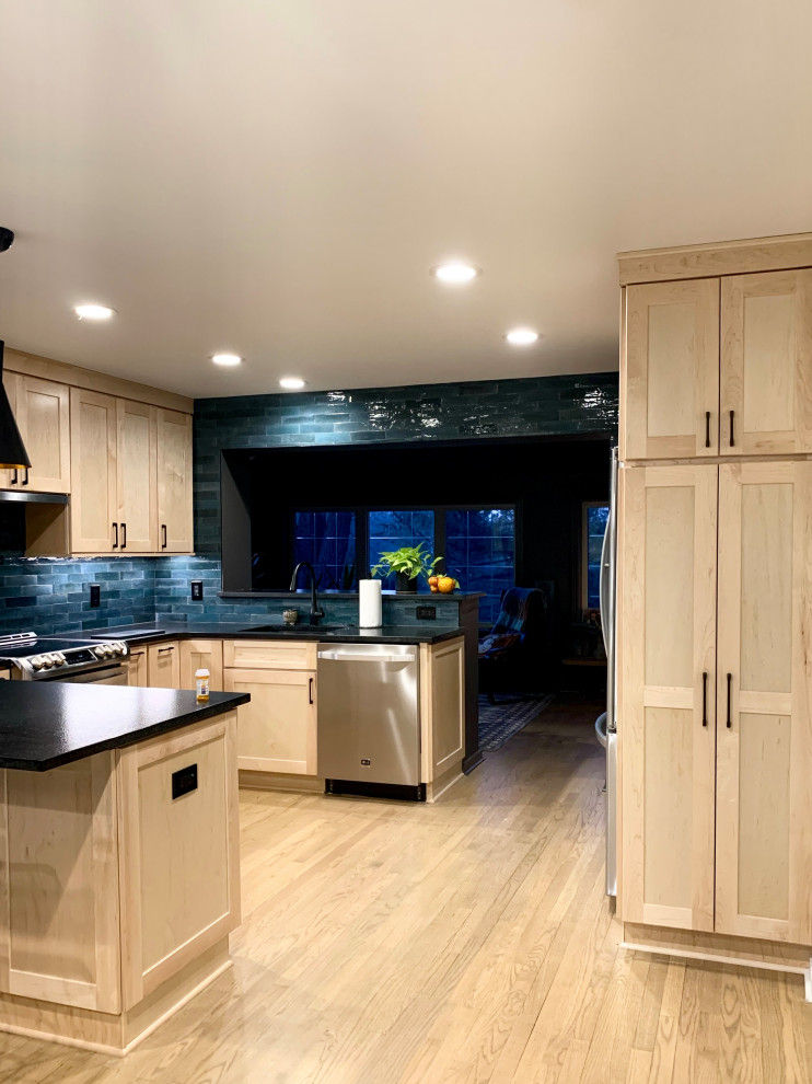 Mid-sized transitional u-shaped light wood floor and brown floor eat-in kitchen photo with an undermount sink, shaker cabinets, light wood cabinets, granite countertops, blue backsplash, ceramic backsplash, stainless steel appliances, a peninsula and black countertops