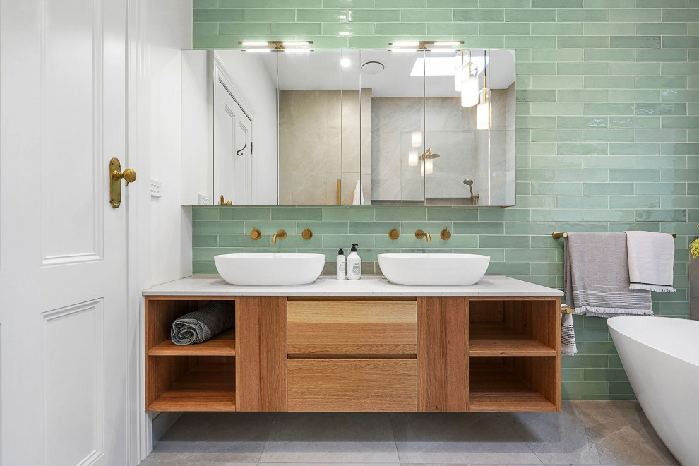 Свежая идея для дизайна: большая главная ванная комната в стиле неоклассика (современная классика) с плоскими фасадами, фасадами цвета дерева среднего тона, отдельно стоящей ванной, душевой комнатой, унитазом-моноблоком, зеленой плиткой, керамической плиткой, серыми стенами, полом из керамогранита, настольной раковиной, столешницей терраццо, серым полом, открытым душем, серой столешницей, нишей, тумбой под две раковины и подвесной тумбой - отличное фото интерьера