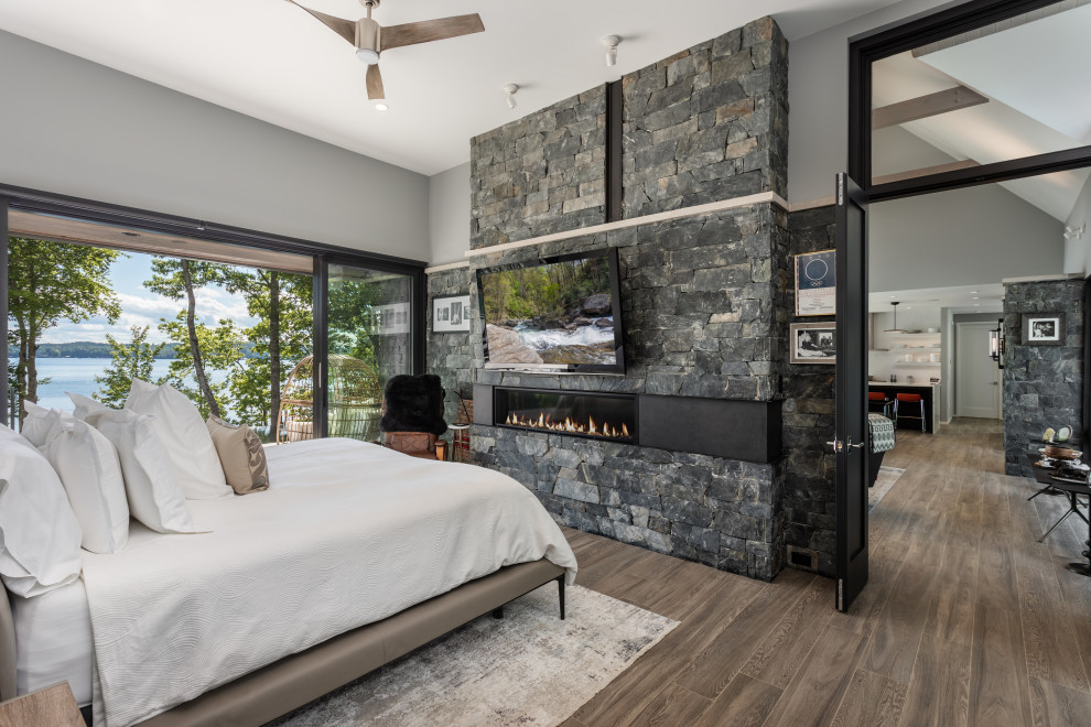 Mittelgroßes Modernes Hauptschlafzimmer mit grauer Wandfarbe, braunem Holzboden, Tunnelkamin und Kaminumrandung aus gestapelten Steinen in Sonstige