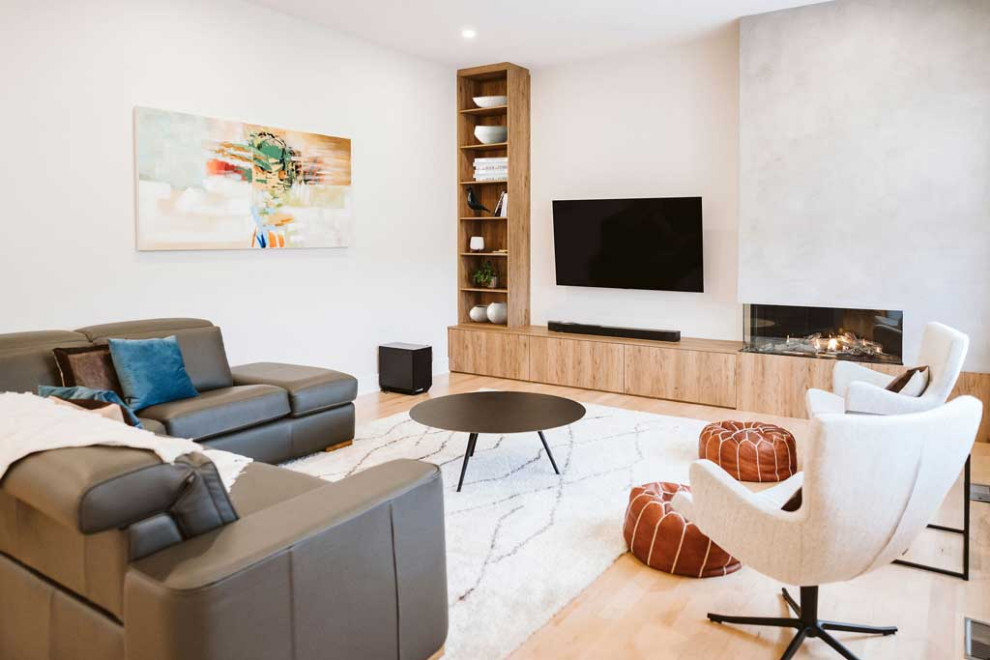 Esempio di un grande soggiorno moderno aperto con pareti beige, parquet chiaro, camino ad angolo, cornice del camino in cemento e TV a parete