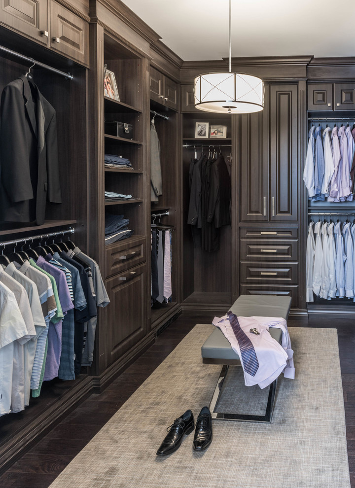 This is an example of a traditional men's walk-in wardrobe in Toronto with raised-panel cabinets, dark wood cabinets, dark hardwood floors and brown floor.