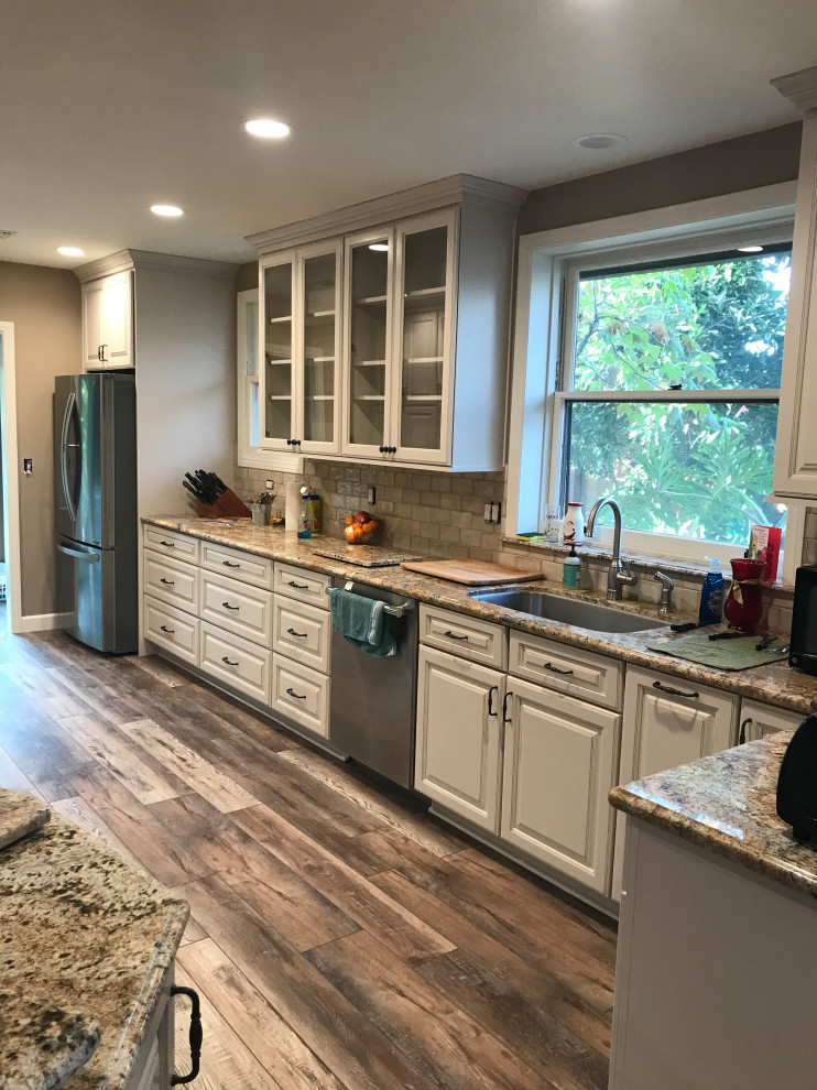 Mid-sized contemporary l-shaped separate kitchen in Los Angeles with an undermount sink, raised-panel cabinets, yellow cabinets, granite benchtops, beige splashback, subway tile splashback, stainless steel appliances, medium hardwood floors, with island, brown floor and brown benchtop.