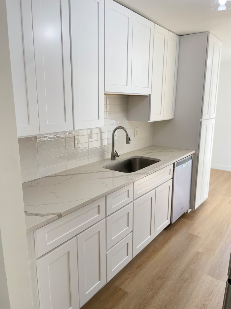 Inspiration for a medium sized contemporary u-shaped kitchen pantry in DC Metro with a submerged sink, shaker cabinets, white cabinets, engineered stone countertops, white splashback, metro tiled splashback, stainless steel appliances, light hardwood flooring, no island, brown floors and white worktops.