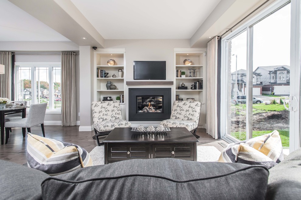 This is an example of a mid-sized transitional formal open concept living room in Toronto with beige walls, medium hardwood floors, a standard fireplace, a plaster fireplace surround and a wall-mounted tv.
