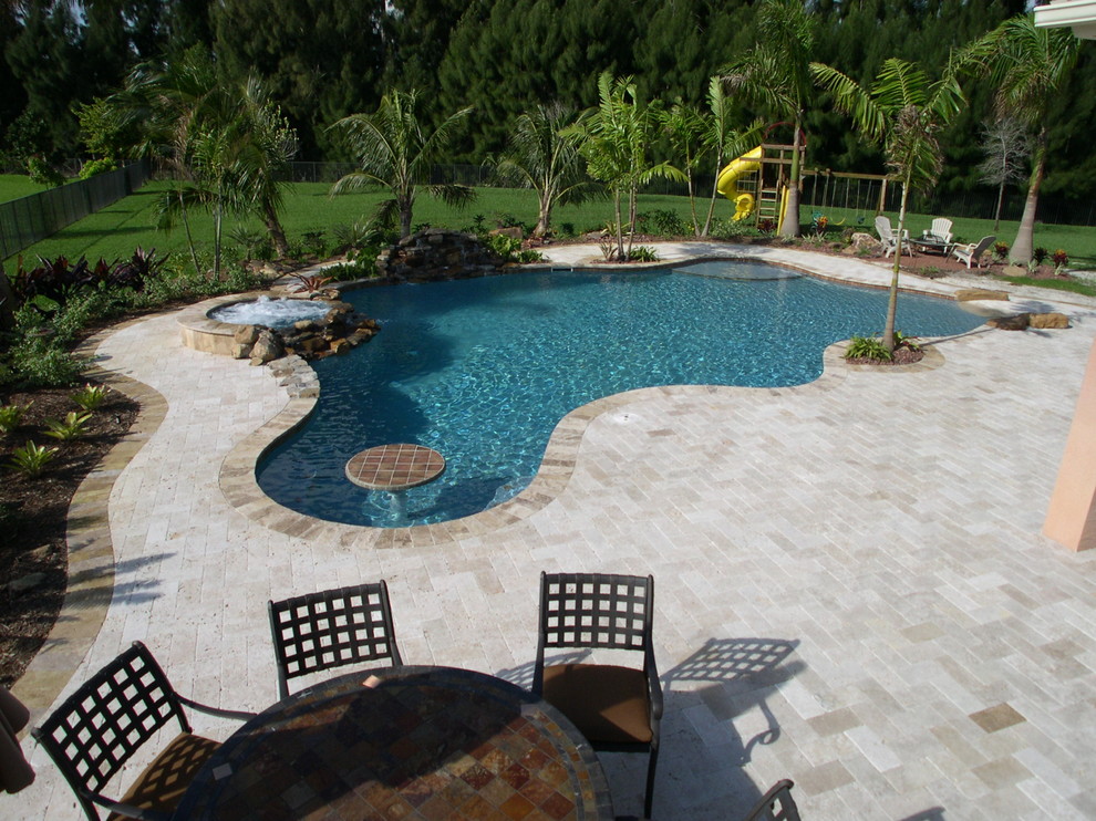 This is an example of a tropical backyard custom-shaped pool in Miami with brick pavers.