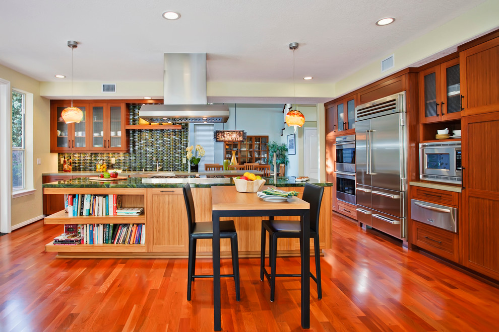 Arts and crafts l-shaped eat-in kitchen in San Diego with shaker cabinets, medium wood cabinets, green splashback, stainless steel appliances, medium hardwood floors, with island and green benchtop.