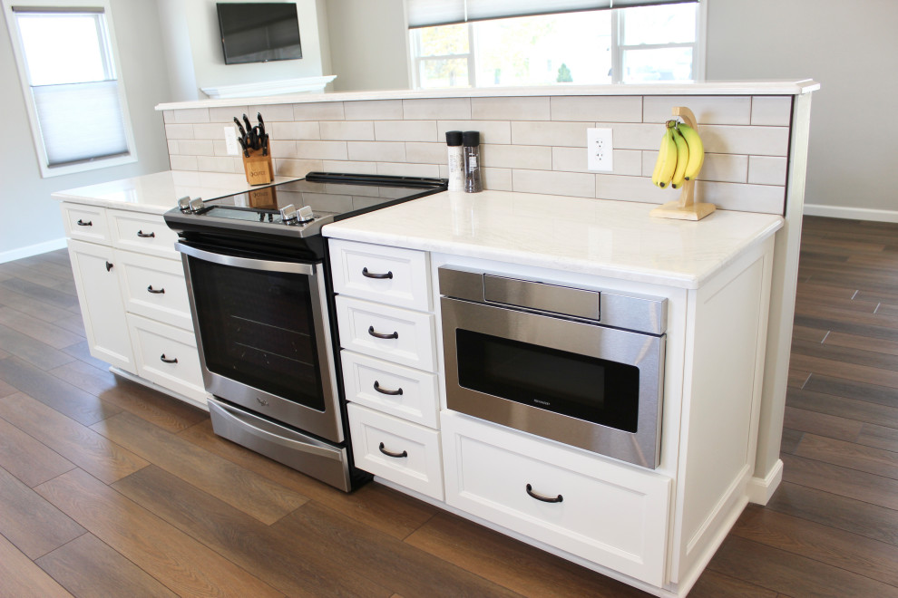 Exempel på ett mellanstort klassiskt vit vitt kök, med en undermonterad diskho, släta luckor, vita skåp, bänkskiva i kvarts, beige stänkskydd, stänkskydd i keramik, rostfria vitvaror, vinylgolv, en köksö och brunt golv