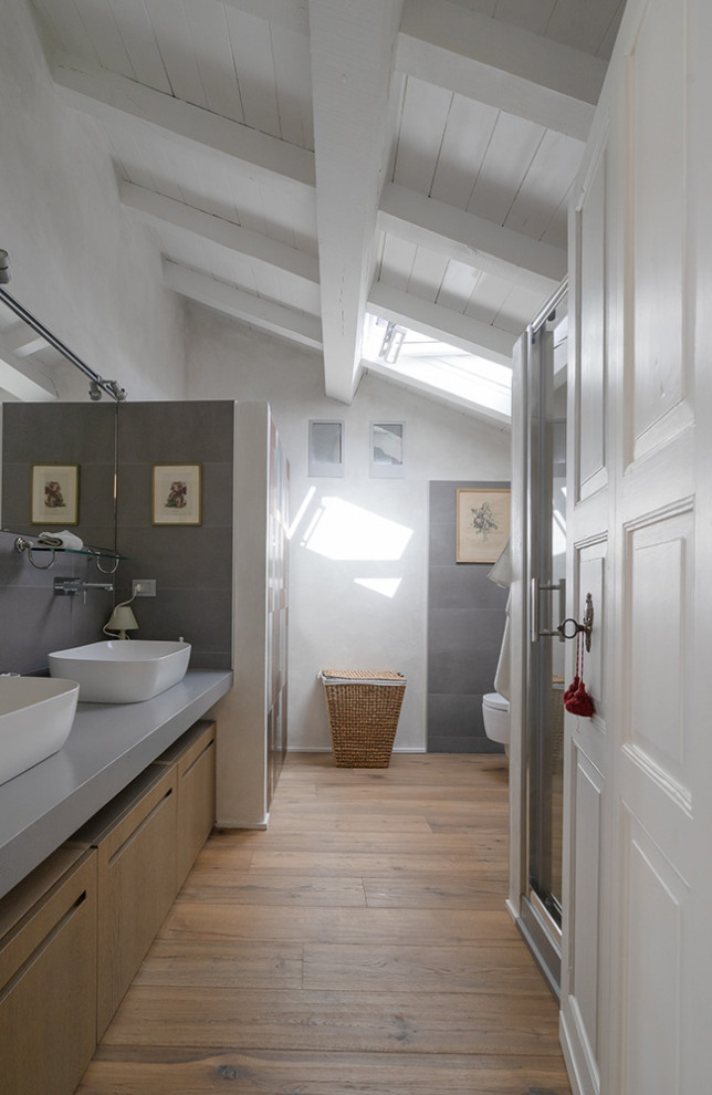 Inredning av ett klassiskt mellanstort grå grått badrum med dusch, med skåp i ljust trä, keramikplattor, grå väggar, ljust trägolv och ett fristående handfat
