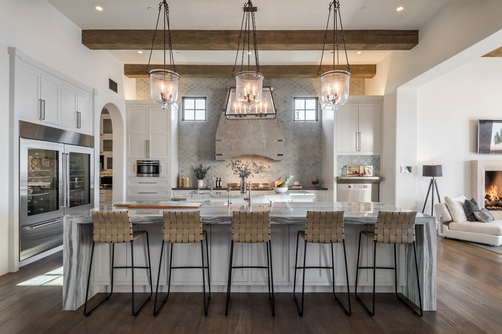 Photo of a mediterranean l-shaped open plan kitchen in Los Angeles with shaker cabinets, white cabinets, grey splashback, dark hardwood floors, with island, brown floor and grey benchtop.