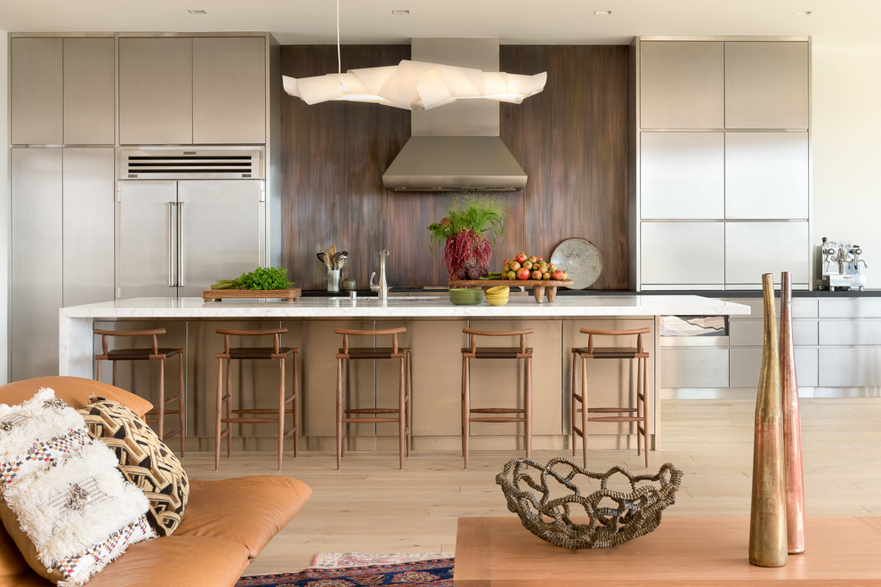 Inspiration for a contemporary galley open plan kitchen in San Francisco with flat-panel cabinets, stainless steel cabinets, brown splashback, stainless steel appliances, light hardwood floors, with island and beige floor.