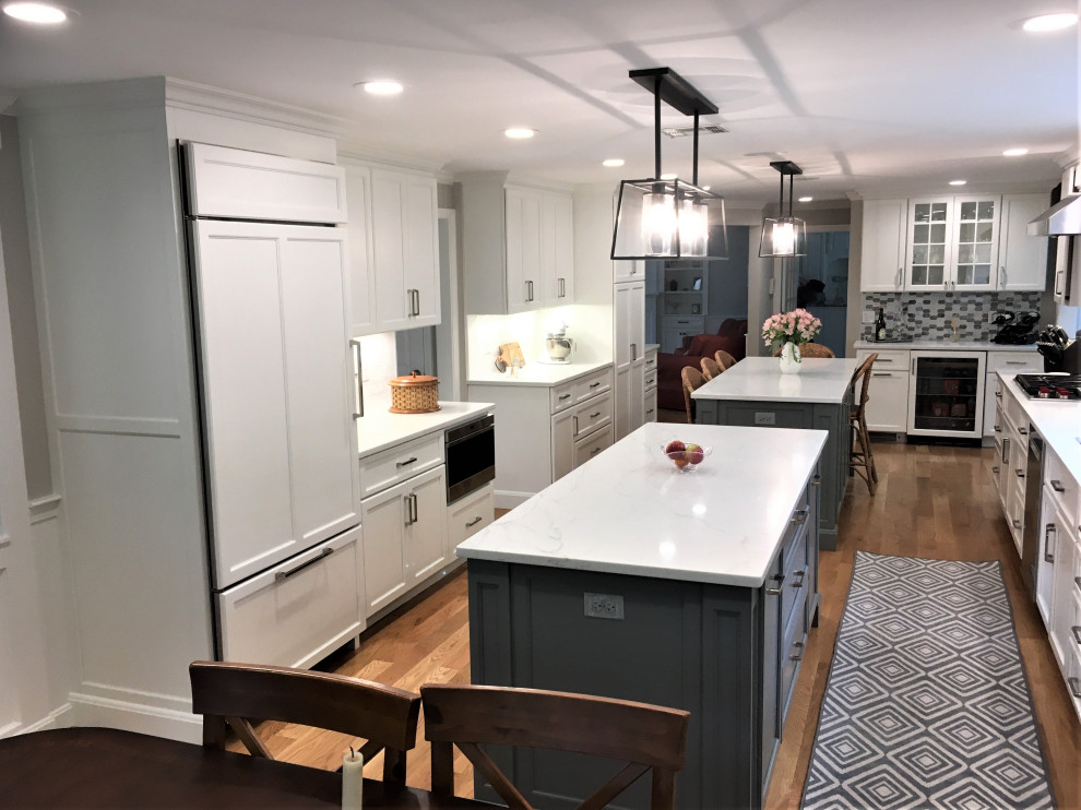 Inspiration for a large transitional galley light wood floor and brown floor eat-in kitchen remodel in Boston with an undermount sink, shaker cabinets, white cabinets, quartz countertops, white backsplash, subway tile backsplash, stainless steel appliances, two islands and white countertops