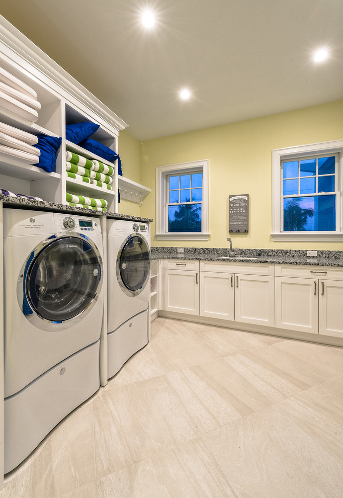 Large transitional u-shaped utility room in Miami with an undermount sink, white cabinets, granite benchtops, yellow walls, ceramic floors and a side-by-side washer and dryer.