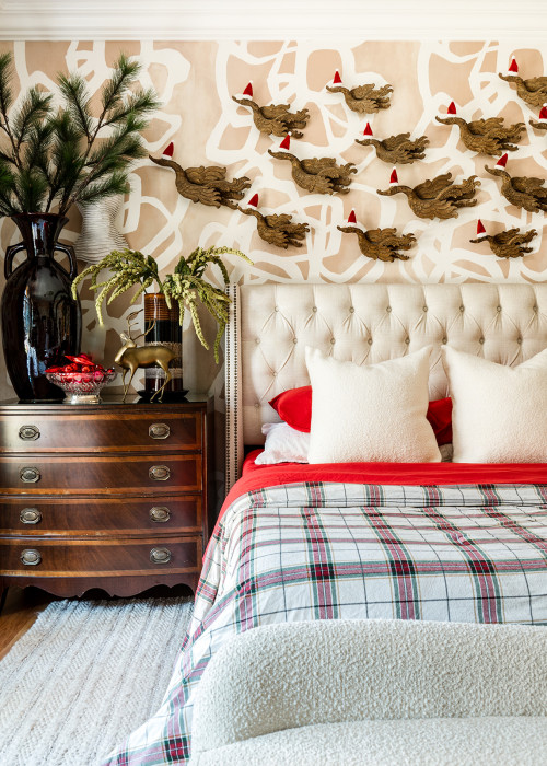 Wooden nightstand styled with greenery, reindeer decor, and holiday candles next to a festive bed.