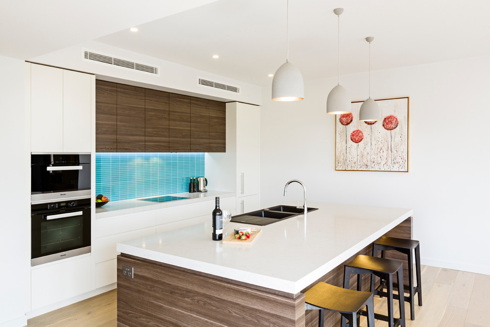 Inspiration for a mid-sized contemporary single-wall eat-in kitchen in Melbourne with a double-bowl sink, flat-panel cabinets, white cabinets, quartz benchtops, blue splashback, ceramic splashback, black appliances, light hardwood floors, with island and beige floor.