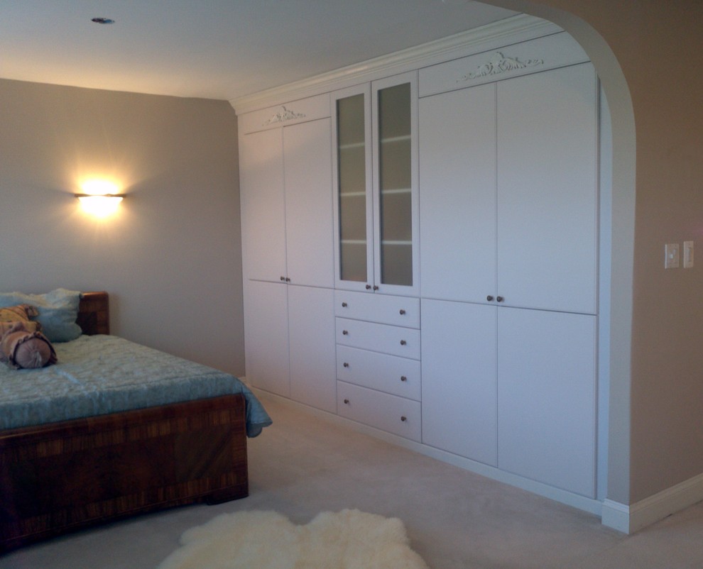 Photo of a small traditional women's built-in wardrobe in DC Metro with white cabinets, carpet and glass-front cabinets.