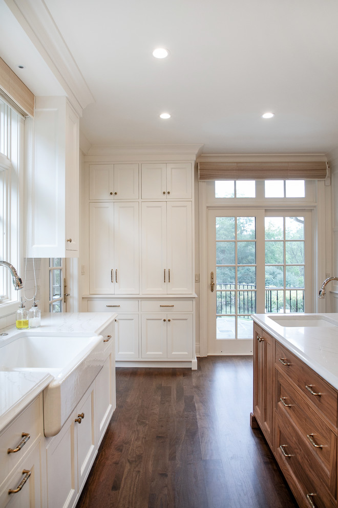 Mid-sized traditional u-shaped separate kitchen in Milwaukee with a farmhouse sink, recessed-panel cabinets, white cabinets, quartz benchtops, white splashback, subway tile splashback, panelled appliances, medium hardwood floors, with island, white benchtop and brown floor.