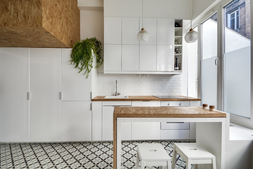 This is an example of a mid-sized contemporary galley open plan kitchen in Paris with a drop-in sink, white cabinets, wood benchtops, brown splashback, subway tile splashback, white appliances, ceramic floors and a peninsula.