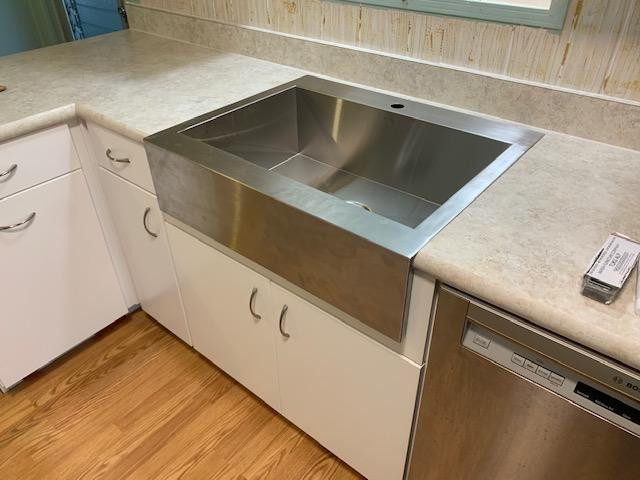 Example of a large u-shaped kitchen pantry design with a farmhouse sink, flat-panel cabinets, white cabinets, laminate countertops, white backsplash, stainless steel appliances, a peninsula and white countertops
