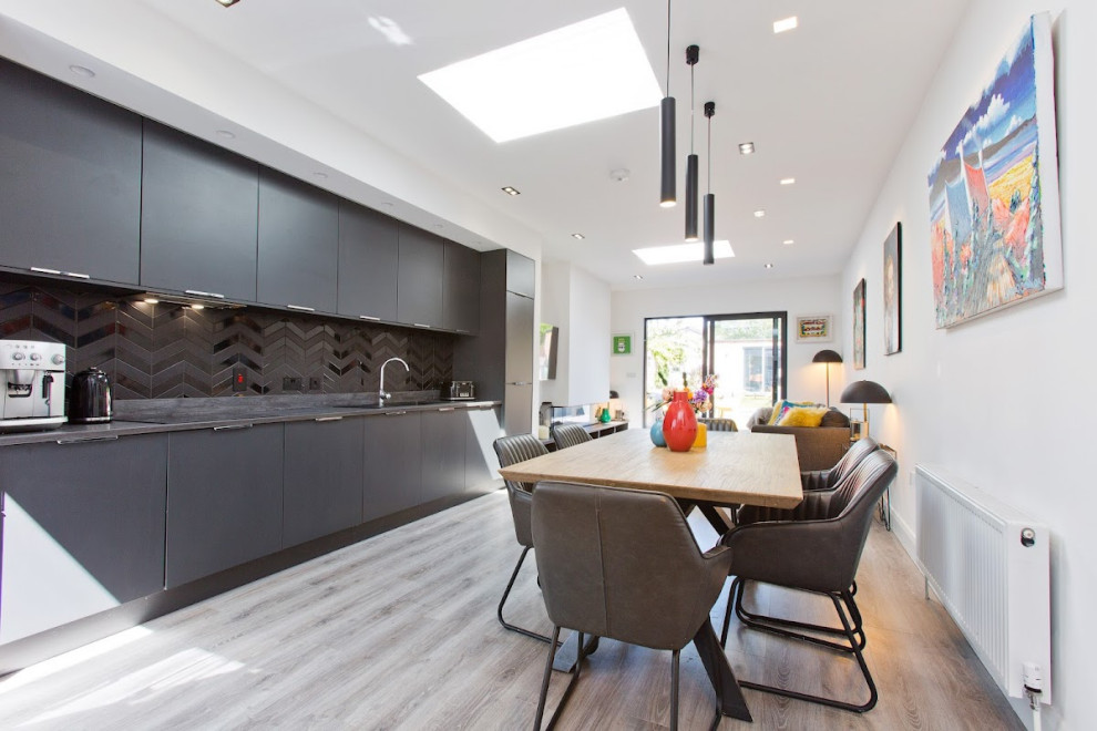 This is an example of a medium sized contemporary single-wall kitchen/diner in Dublin with a built-in sink, flat-panel cabinets, black cabinets, composite countertops, black splashback, metro tiled splashback, black appliances, laminate floors, no island and black worktops.