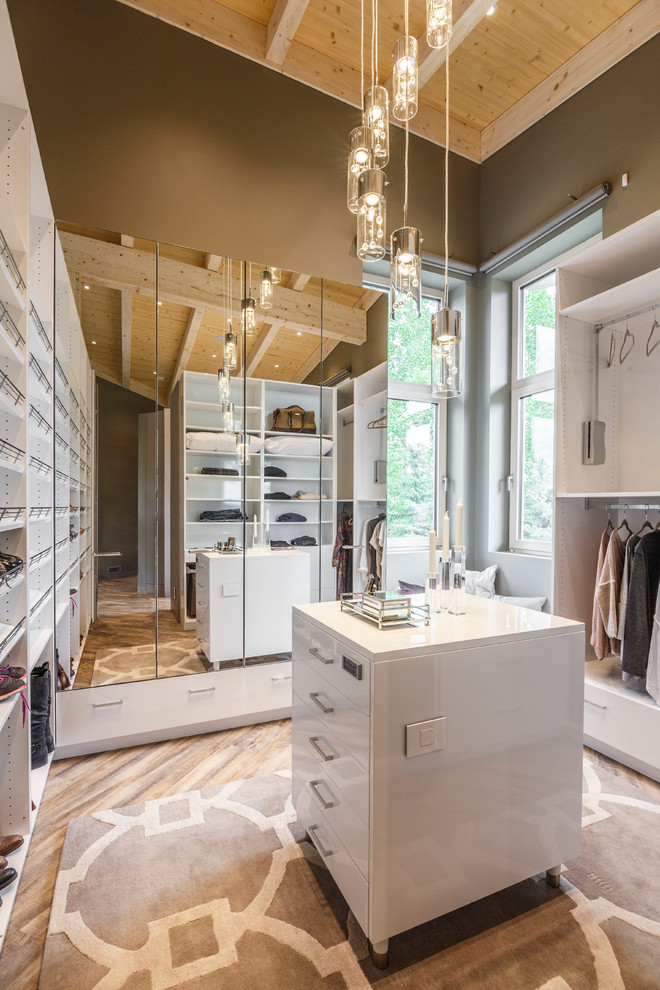 This is an example of a contemporary walk-in wardrobe in Other with flat-panel cabinets, white cabinets, brown floor and medium hardwood floors.