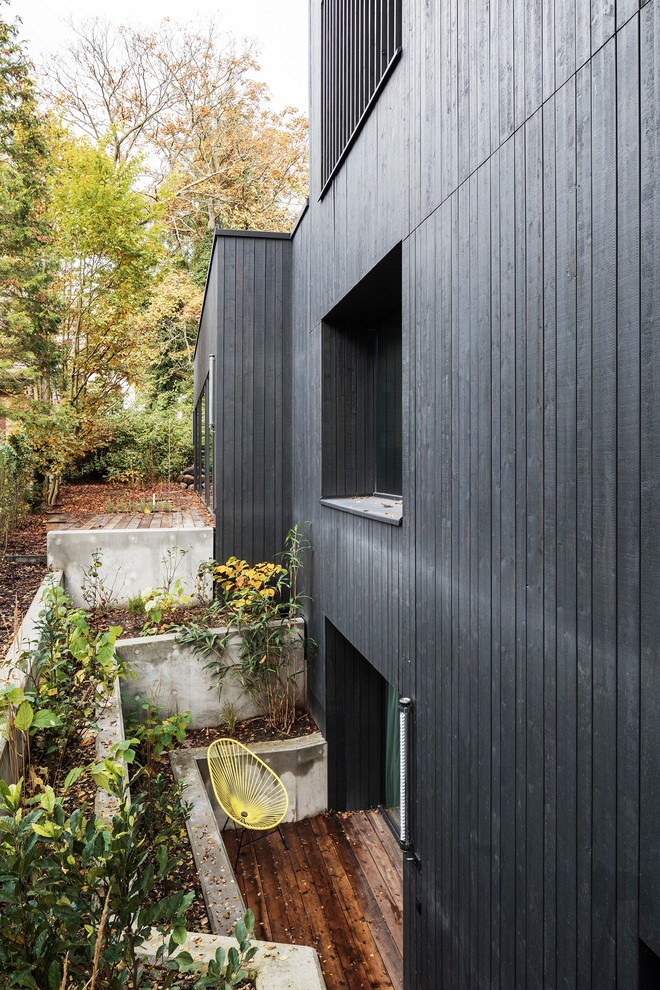 Design ideas for a mid-sized industrial two-storey black house exterior in Berlin with wood siding and a flat roof.
