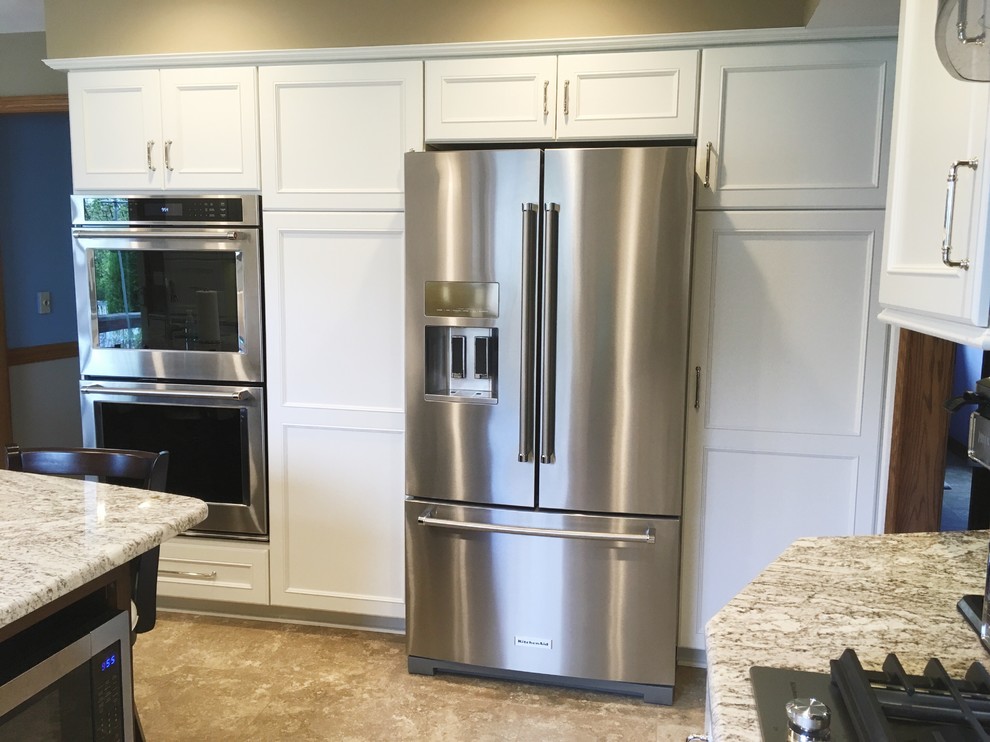 Example of a large transitional l-shaped vinyl floor and beige floor eat-in kitchen design with a double-bowl sink, recessed-panel cabinets, white cabinets, granite countertops, brown backsplash, ceramic backsplash, stainless steel appliances and an island