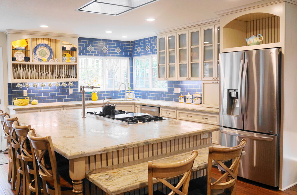 Mid-sized mediterranean l-shaped open plan kitchen in San Diego with an undermount sink, glass-front cabinets, white cabinets, limestone benchtops, blue splashback, subway tile splashback, stainless steel appliances, medium hardwood floors, with island and brown floor.
