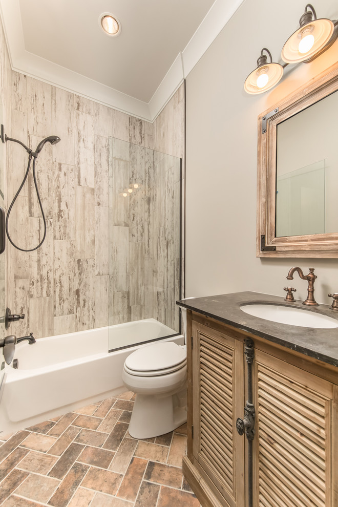 Mid-sized industrial bathroom in Other with louvered cabinets, light wood cabinets, an alcove tub, a shower/bathtub combo, a two-piece toilet, gray tile, porcelain tile, grey walls, brick floors, an undermount sink and concrete benchtops.