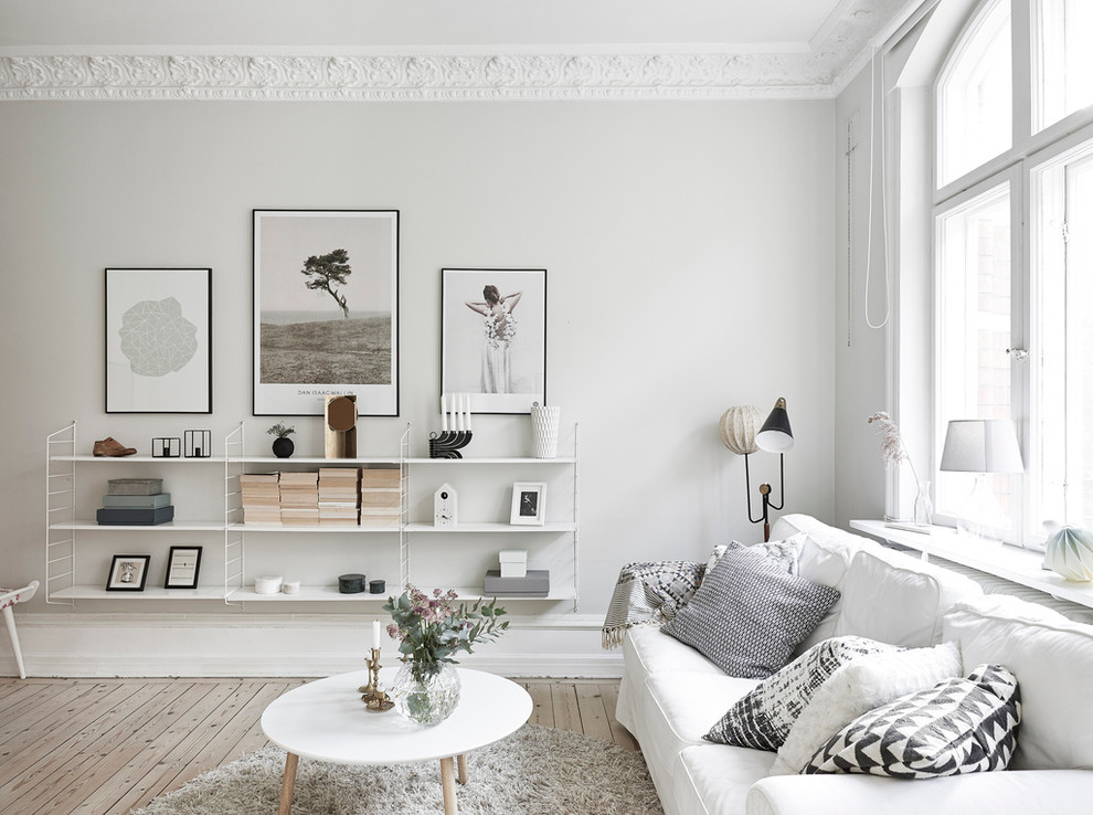 This is an example of a mid-sized scandinavian enclosed living room in Gothenburg with a library, white walls, light hardwood floors and no fireplace.