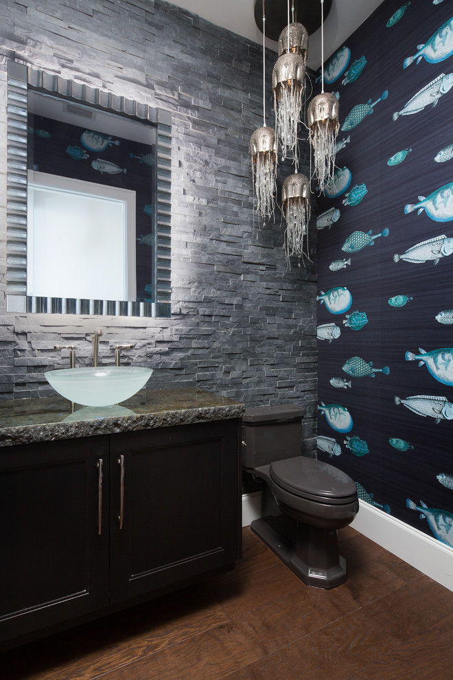 Photo of a mid-sized tropical powder room in Miami with recessed-panel cabinets, dark wood cabinets, gray tile, stone tile, a vessel sink, granite benchtops, a two-piece toilet, multi-coloured walls, dark hardwood floors and brown floor.