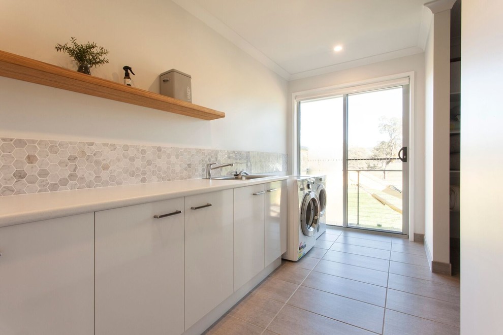 Inspiration for a large contemporary single-wall dedicated laundry room in Other with a drop-in sink, laminate benchtops, white walls, ceramic floors, a side-by-side washer and dryer, grey floor and white benchtop.