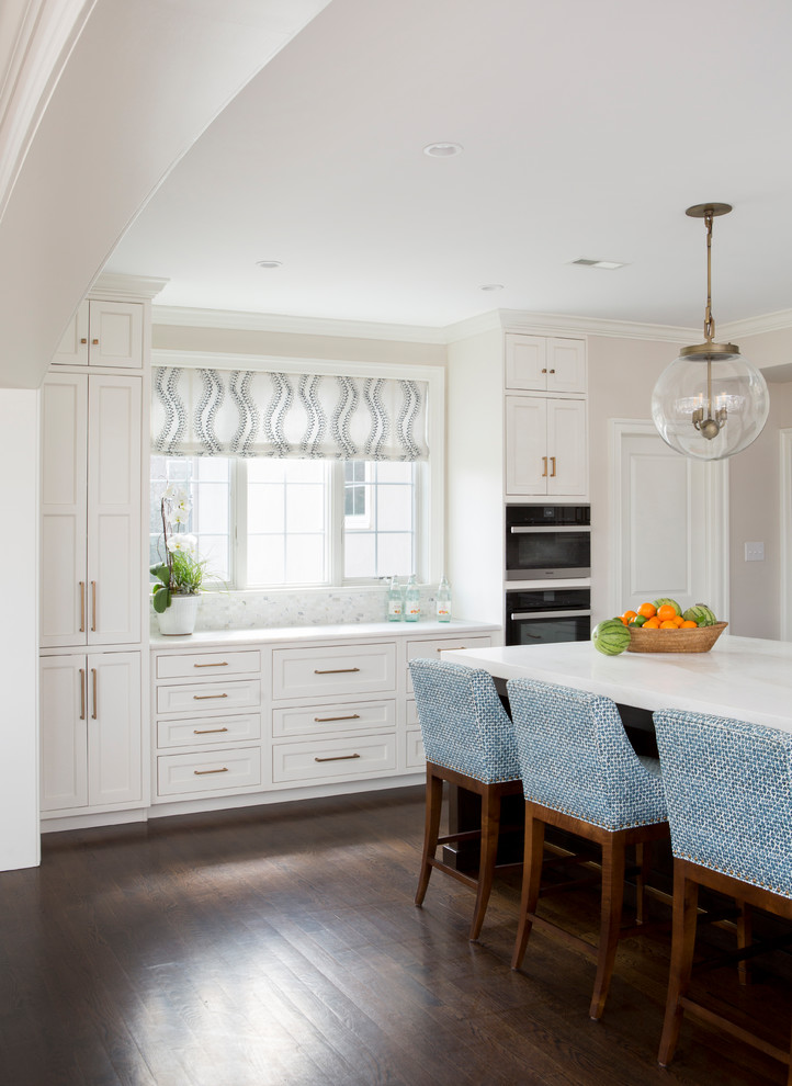 Mid-sized transitional u-shaped open plan kitchen in Philadelphia with an undermount sink, beaded inset cabinets, white cabinets, quartzite benchtops, white splashback, marble splashback, stainless steel appliances, dark hardwood floors, with island, brown floor and white benchtop.