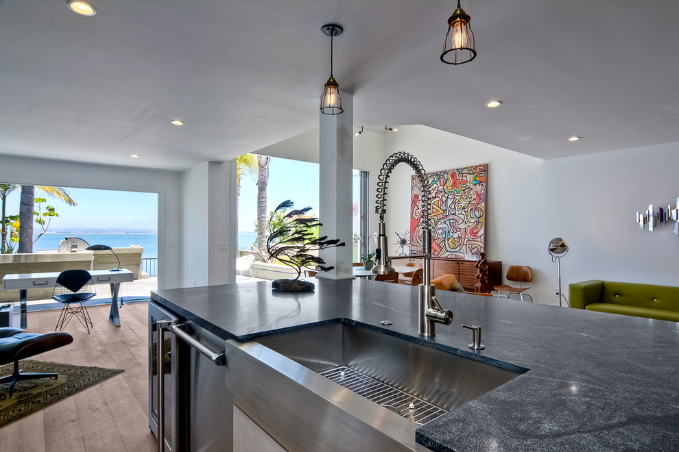 Inspiration for a modern single-wall open plan kitchen in San Diego with a farmhouse sink, flat-panel cabinets, grey cabinets, marble benchtops, white splashback, subway tile splashback, stainless steel appliances, light hardwood floors and with island.