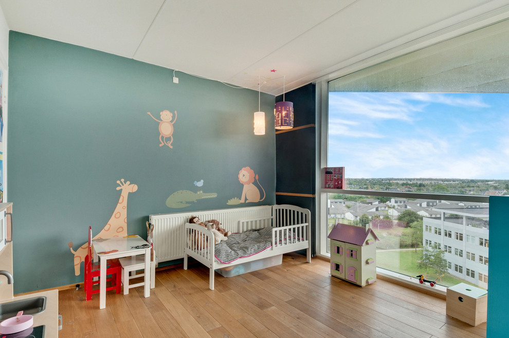 Photo of a mid-sized contemporary gender-neutral kids' room in Copenhagen with blue walls and light hardwood floors.