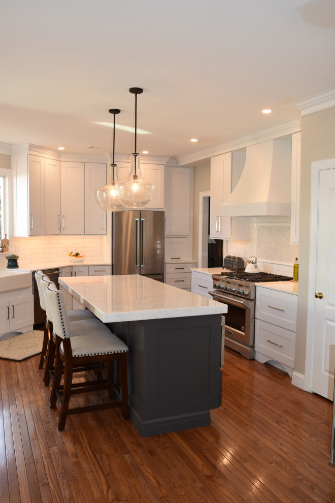 This is an example of a large transitional u-shaped eat-in kitchen in Philadelphia with a farmhouse sink, recessed-panel cabinets, white cabinets, quartzite benchtops, white splashback, subway tile splashback, stainless steel appliances, medium hardwood floors, with island, brown floor and white benchtop.