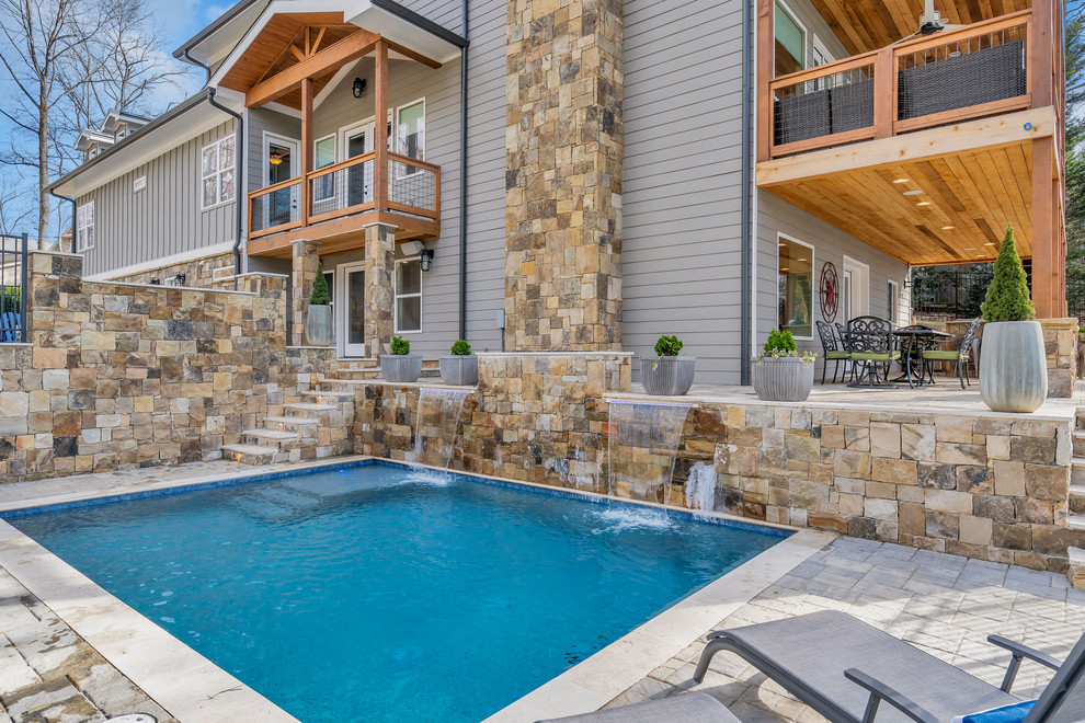 This is an example of a mid-sized arts and crafts backyard rectangular lap pool in Other with a water feature and natural stone pavers.