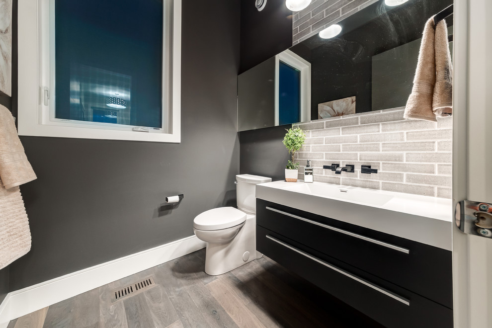 Trendy beige tile and porcelain tile medium tone wood floor bathroom photo in Calgary with flat-panel cabinets, dark wood cabinets, a two-piece toilet, gray walls, a console sink and solid surface countertops