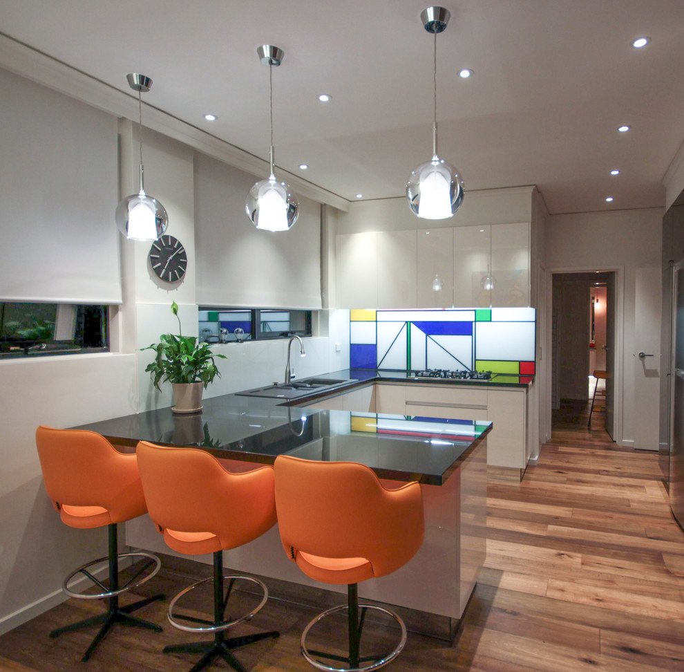 Photo of a mid-sized contemporary u-shaped eat-in kitchen in Melbourne with flat-panel cabinets, white cabinets, granite benchtops, multi-coloured splashback, light hardwood floors and no island.