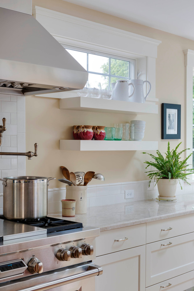 Example of a large transitional l-shaped light wood floor kitchen design in Boston with a farmhouse sink, recessed-panel cabinets, white cabinets, quartz countertops, white backsplash, subway tile backsplash, stainless steel appliances and an island