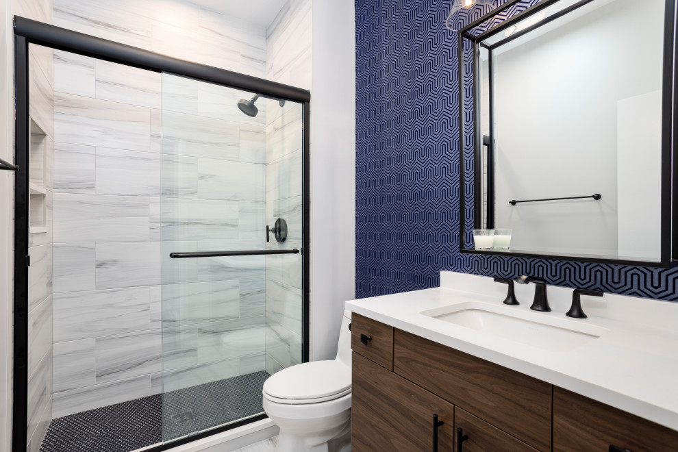 Photo of a contemporary shower room bathroom in Chicago with a two-piece toilet, white walls, mosaic tile flooring, black floors, a sliding door, a wall niche, medium wood cabinets, an alcove shower, porcelain tiles, engineered stone worktops, white worktops, a single sink, grey tiles and a submerged sink.